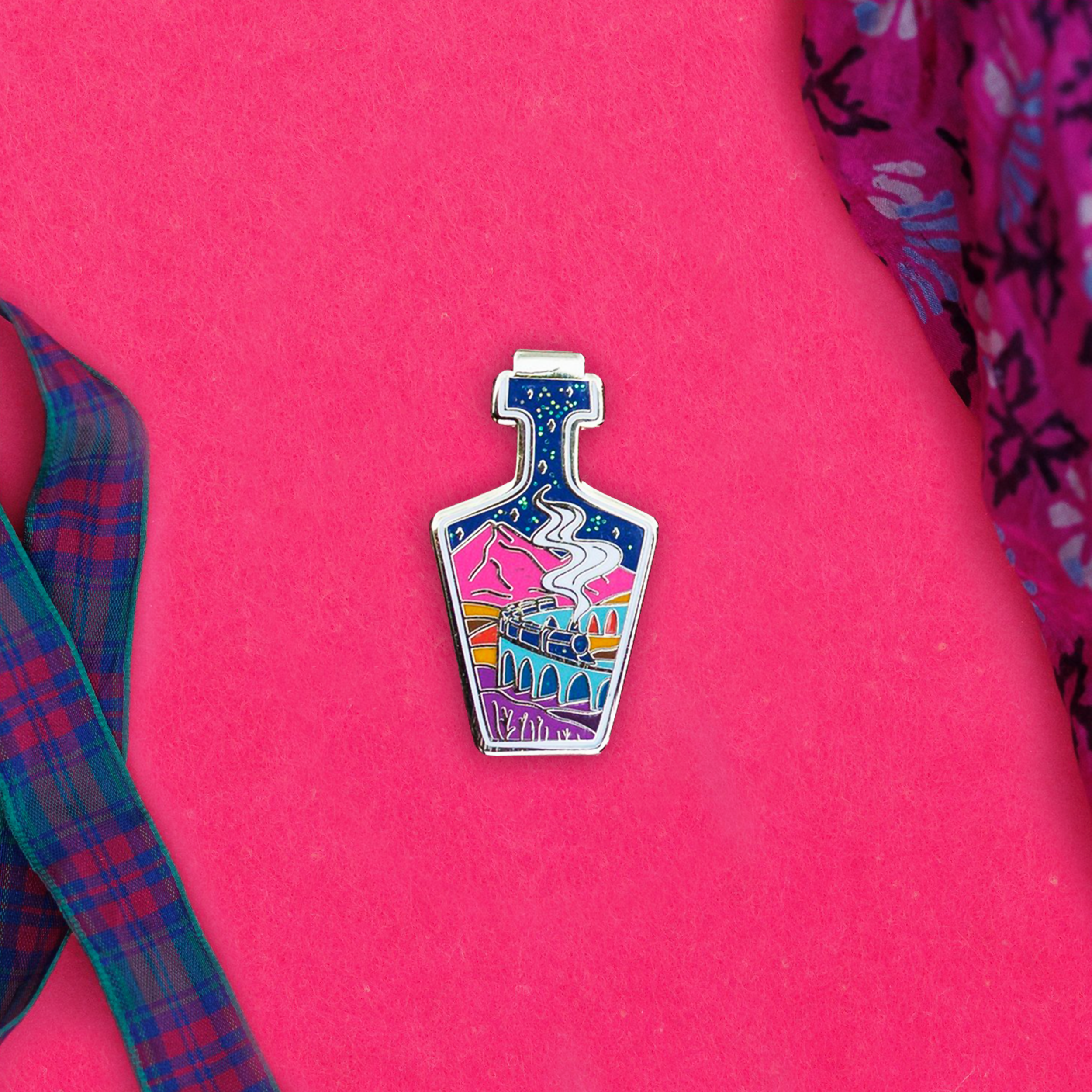 Enamel pin with whimsical design on a pink background.