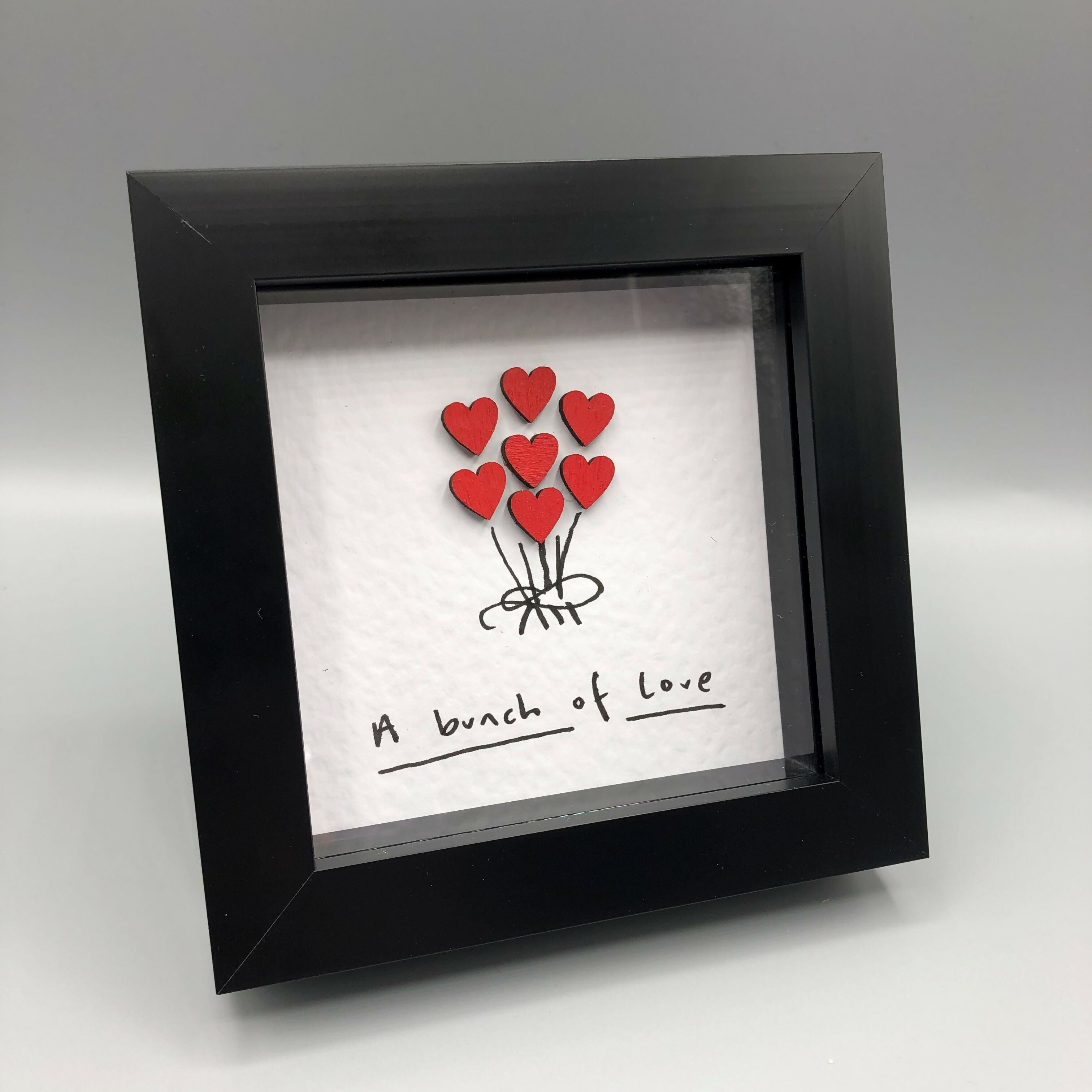 A bouquet of red hearts in a small black frame.