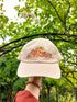 Beige coloured cap with orange embroidered mountain range on.