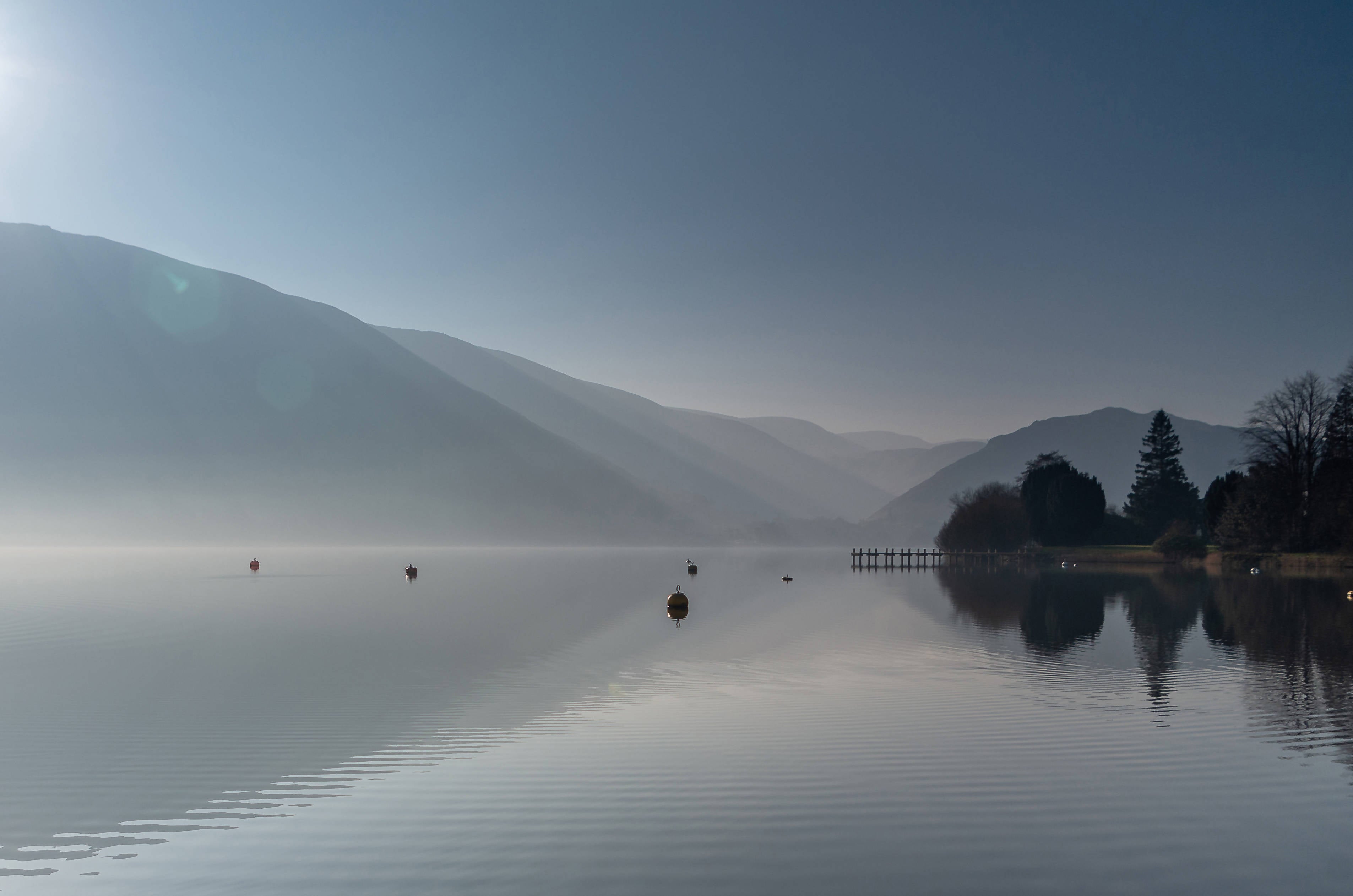 Calm photograph of Ullswater lake with misty mountains behind.