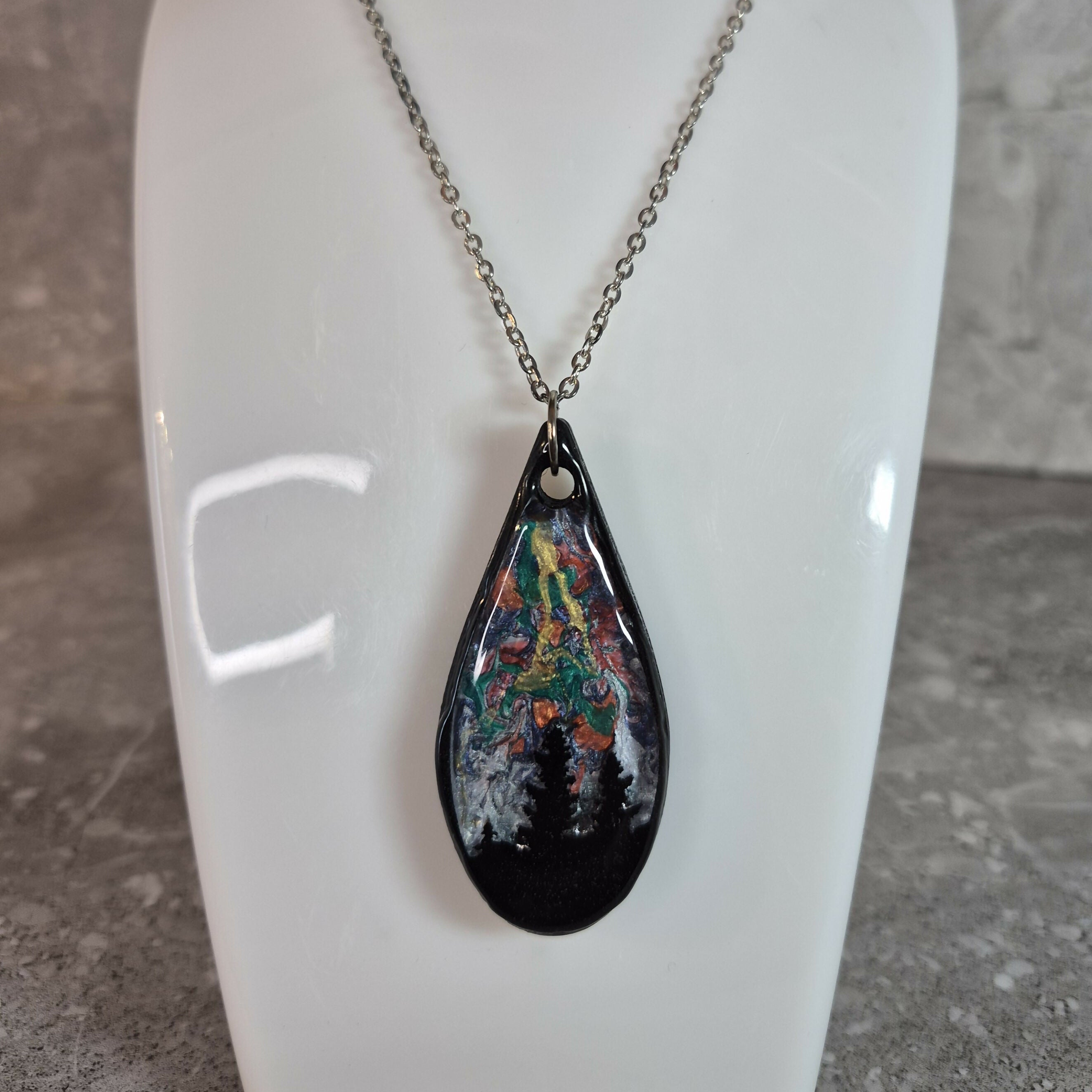 Unique, Hand Crafted, Teardrop Pendant Showing Black Silhouetted Pine Trees Against a Multicoloured Abstract Back Ground Sky