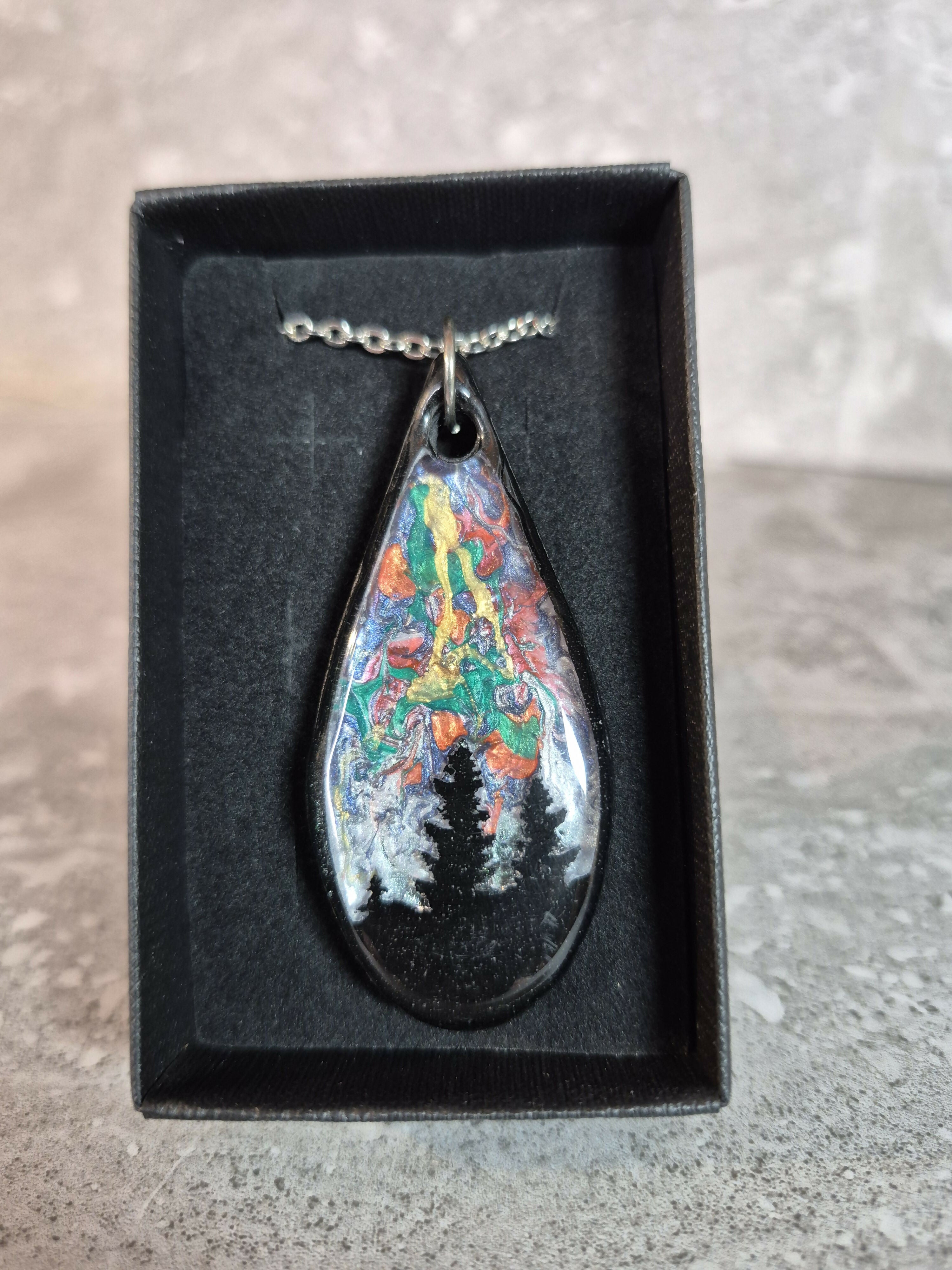 Unique, Hand Crafted, Teardrop Pendant Showing Black Silhouetted Pine Trees Against a Multicoloured Abstract Back Ground Sky