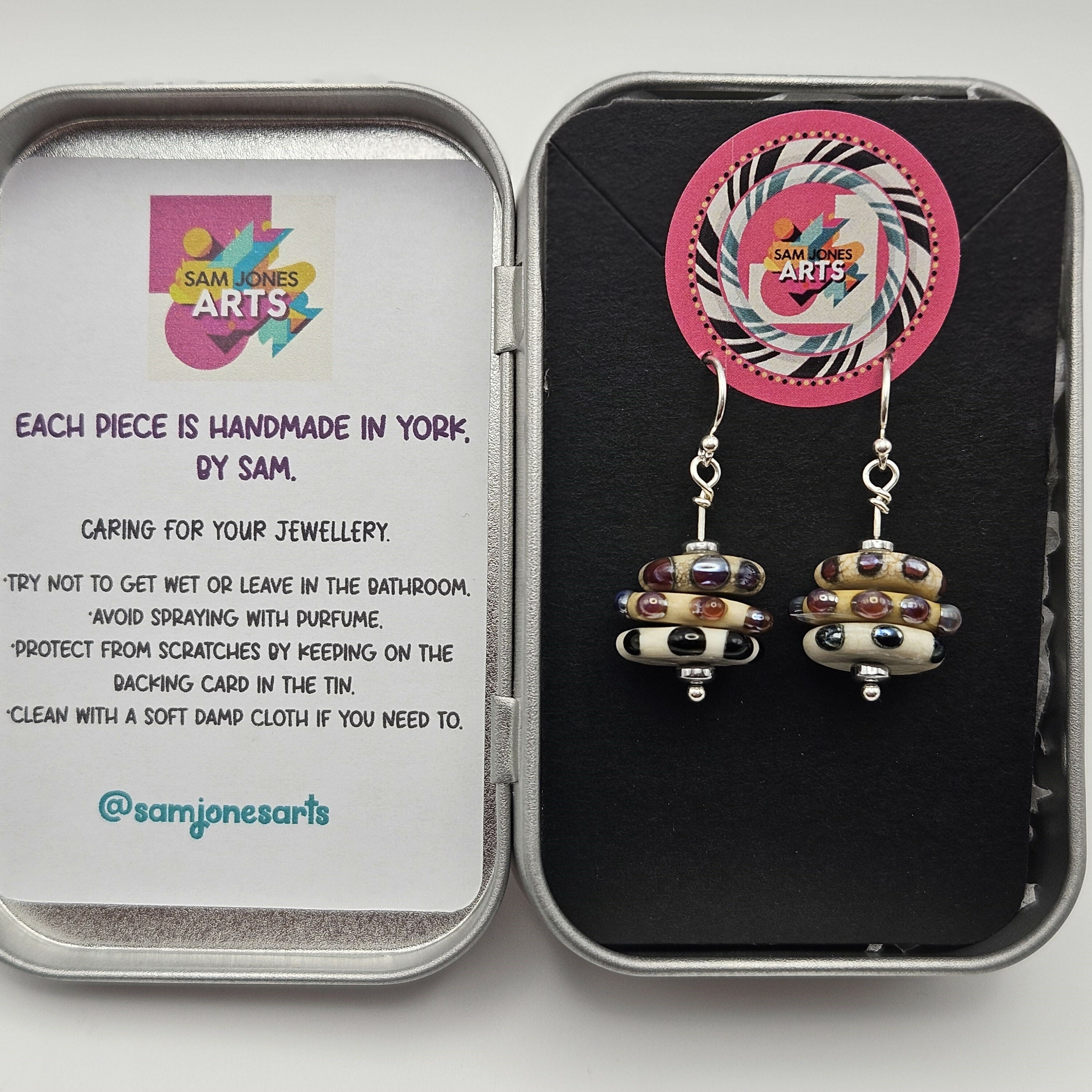 HAND LAMP WORKED GLASS STACKED EARRINGS, WITH DOTS AND SPOTS, STERLING SILVER EAR WIRES AND HEMATITE ACCENT BEADS.